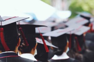 A photo of graduates walking in a line away from the camera. Close up of shoulders, back of heads and graduation caps with red tassels.